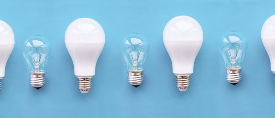 Energy-saving lamps with incandescent lamps in a row on a blue background. The concept of saving energy.