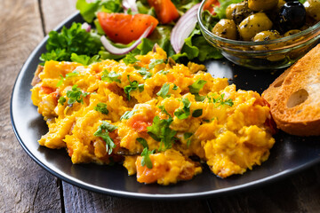 Breakfast - scrambled eggs with vegetables and toasted bread on wooden background