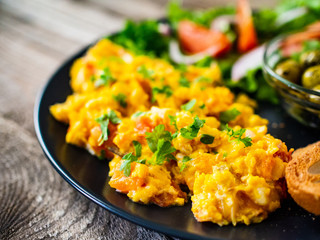 Breakfast - scrambled eggs with vegetables and toasted bread on wooden background