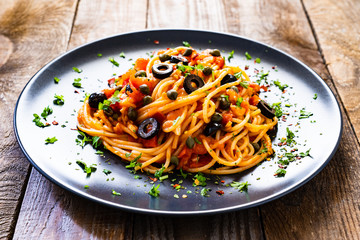 Pasta puttanesca with tomato sauce, anchovies, chilli, capers and olives on wooden table