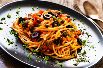 Pasta puttanesca with tomato sauce, anchovies, chilli, capers and olives on wooden table