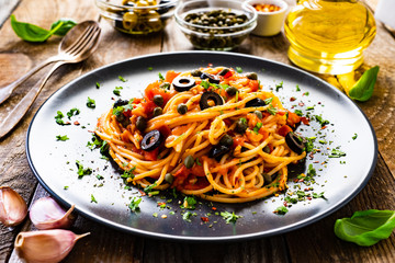 Pasta puttanesca with tomato sauce, anchovies, chilli, capers and olives on wooden table