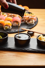 Hand  pouring soy sauce (Shoyu) from little jug into the bowl before eating japanese food such as sushi roll