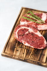 Raw meat beef steak, with ingredients for cooking on a wooden board and white background. Top view