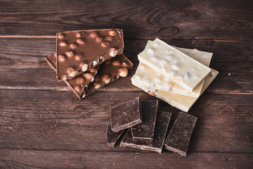 Dark and white chocolate with nuts, dark chocolate on a dark wooden background. Broken into pieces sweet dessert top view.