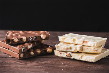 Dark and white chocolate with nuts broken into pieces on a dark wooden background. Tower of chocolate.