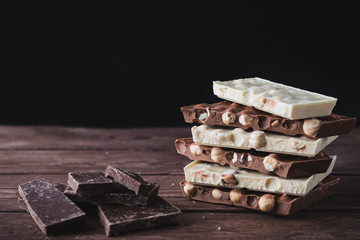 Dark and white chocolate with nuts broken into pieces on a dark wooden background. Tower of chocolate.