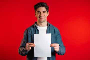 Handsome man holding vertical white a4 paper poster. Copy space. Smiling hipster guy in shirt on...