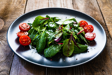 Vegetable salad - green leaves and cherry tomatoes on wooden table