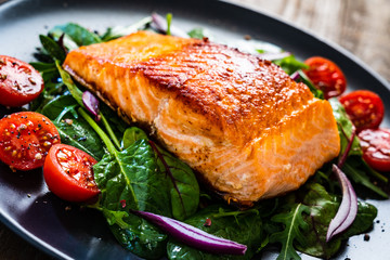 Fried salmon steak with vegetables on wooden table