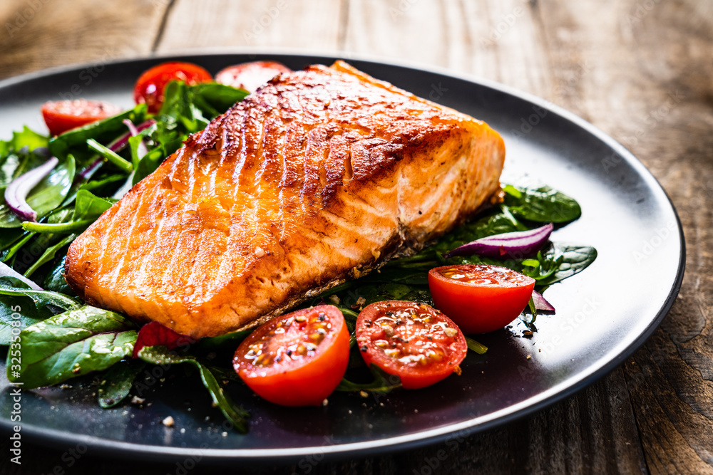 Wall mural Fried salmon steak with vegetables on wooden table