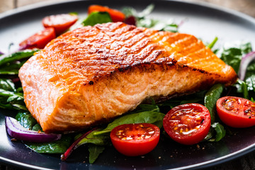 Fried salmon steak with vegetables on wooden table