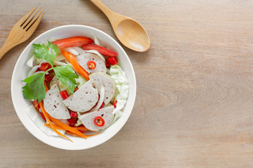 top view  of spicy vietnamese pork sausage salad in a ceramic bowl on wooden table. delicious asian...