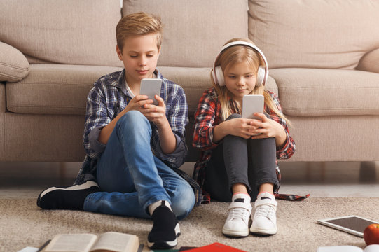 Siblings Using Mobile Phones Playing Games Sitting On Floor Indoor