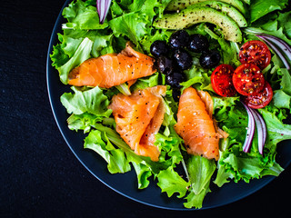 Salmon salad - smoked salmon and vegetables on black stone background