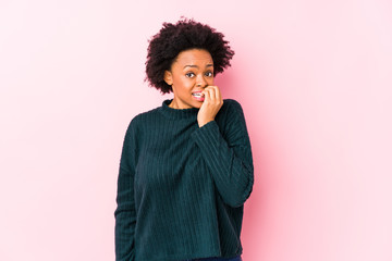 Middle aged african american woman against a pink background isolated biting fingernails, nervous...