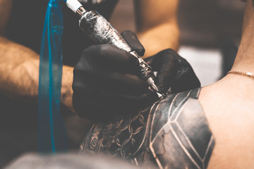 Tattoo salon. The tattoo master is tattooing a man on his shoulder. Tattoo machine, safety and...