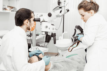 Two dentists treat a patient. Using the camera and photographing in dentistry. Professional uniform and equipment of a dentist. Healthcare Equipping a doctor’s workplace. Dentistry
