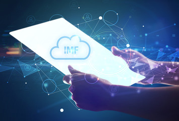 Hand holdig futuristic tablet with IMF inscription, modern technology concept
