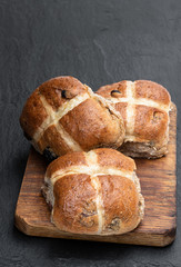 Easter wholemeal hot cross buns on wooden board on black stone background