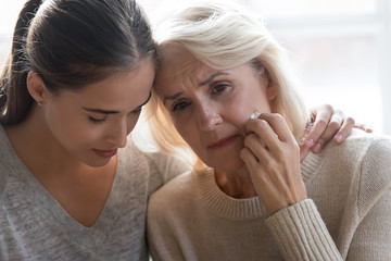 Close up young grown up worried daughter hugging frustrated mother.