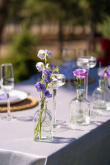 Decorative decoration of the festive table. Glass vases and fresh flowers. Decoration of holidays in the open air