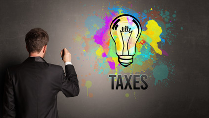 businessman drawing colorful light bulb with TAXES inscription on textured concrete wall, new business idea concept
