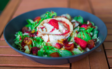 Delicious salad with goat cheese and strawberries served on wooden background
