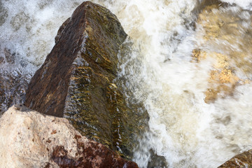 Large cobble stones washed by mountain water in fast river.