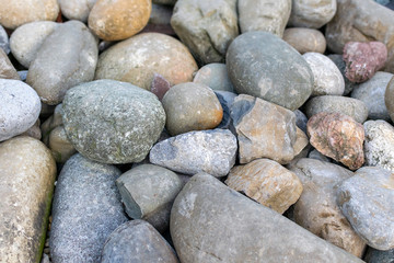 Natural background of a pile of big rocks or pebbles on the seashore close-up. The surface of the beach on the ocean is covered with large polished round stones of gray color of different sizes.