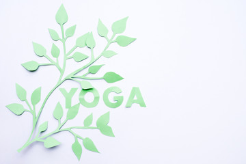 word YOGA made of paper with green leaves on white background