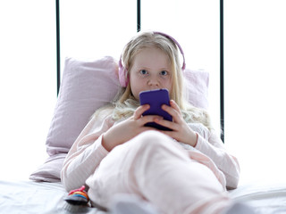 modern life of generation Z. teenage girl in pajamas and headphones in the room on the bed listens to music from a smartphone.