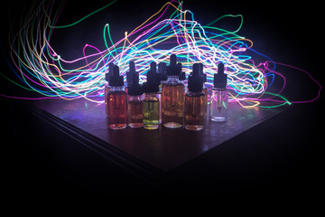 Smoke clouds and vape liquid bottles on dark background. Light effects. Useful as background or...