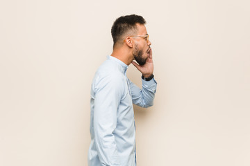 Young south-asian business man shouting and holding palm near opened mouth.