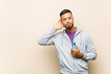 Young mixed race asian man holding a water bottle trying to listening a gossip.