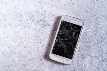 Broken mobile phone with cracked display on concrete background, flat lay.