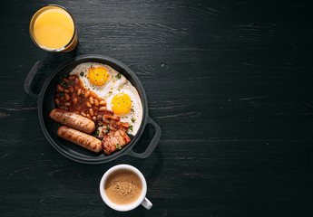 English breakfast on a dark table. fried eggs with bacon canned beans and sausage. near coffee,...