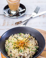 A serving of Mushroom Risotto in a dark round bowl, with a knife and fork, and cup of coffee in the background