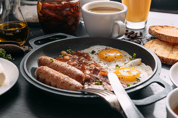 English breakfast on a dark table. fried eggs with bacon canned beans and sausage. near coffee, orange juice and pancakes with butter and honey