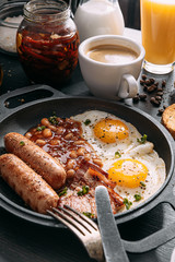 English breakfast on a dark table. fried eggs with bacon canned beans and sausage. near coffee, orange juice and pancakes with butter and honey