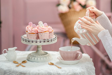Tea party. The girl pours tea into a pink mug. Set table. Tea party with cupcakes