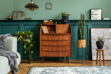 Stylish interior design with retro wooden cabinet, chair,  mint sofa, plants, pendant lamp, decoratnion, maps, stool and elegant personal accessories. Modern retro concept of home office space. 