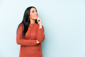 Young caucasian woman isolated on a blue background looking sideways with doubtful and skeptical expression.