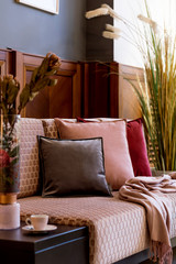 Stylish interior of living room with design pink sofa, elegant pillows, plaid, flowers decoration and elegant personal accessories. Modern home decor.  Clos up. Wood panelling. Details. Template.  