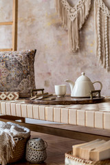 Interior design of stylish living room with beige chaise longue, beautiful macrame, pillow ladder, books, tea pot on the tray and elegant personal accessories. Oriental concept of home decor. Template