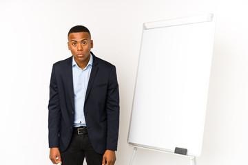Young latin man with a white board isolated on a white background shrugs shoulders and open eyes...