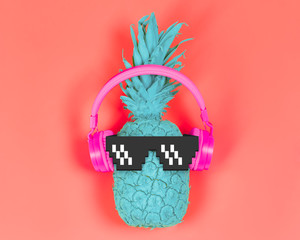 Pineapple in pink headphones and pixel glasses on a coral background