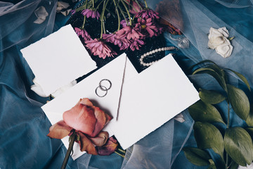 Wedding invitation mockup with roses, old cracked, rings, papers on white textile background. Top view, flat lay. Wedding stationary. Perfect for presentation of your invitation, menu, greeting cards