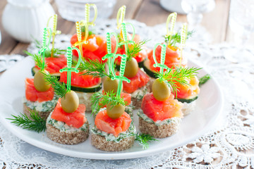 assorted canapes with salmon on white and black bread on a white plate, selective focus