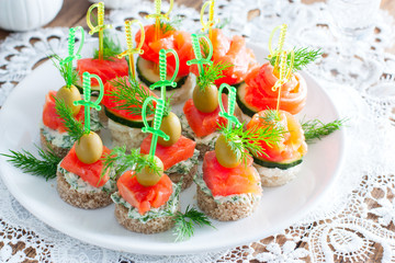 assorted canapes with salmon on white and black bread on a white plate, selective focus